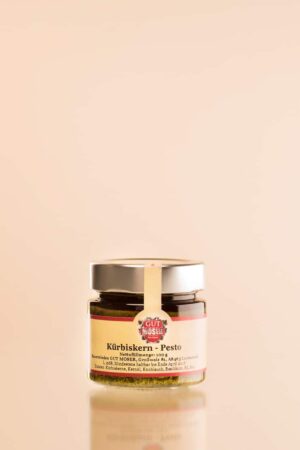 Das große Kürbiskernpesto-Glas mit dem Markennamen und den Details in deutscher Sprache steht auf einem beigen Hintergrund. Es hat einen silbernen Deckel mit einem weiß-roten Band um den oberen Rand.