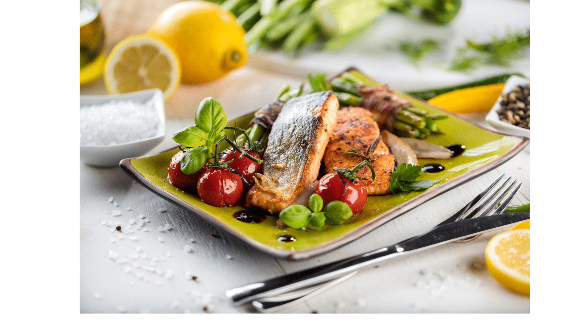 Gegrillte Lachsfilets mit Kirschtomaten, frischen Kräutern und Blattgemüse auf einem grünen Teller, dazu Zitrone, Salz und Besteck.