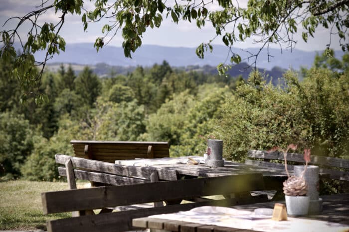 Holz-Picknicktische im Freien mit Blick auf einen Wald und ferne Hügel.